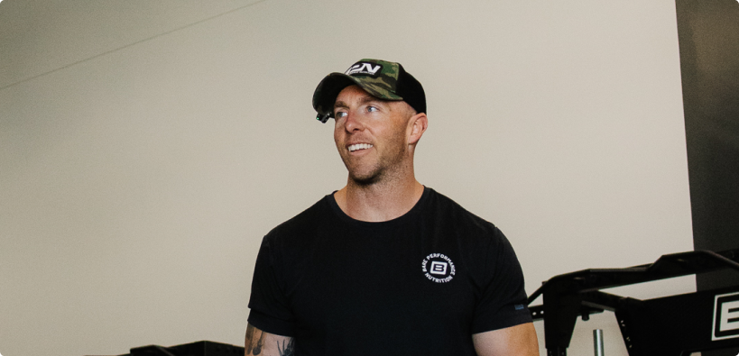 A man in a black t-shirt and camouflage hat looking off to the side and smiling.