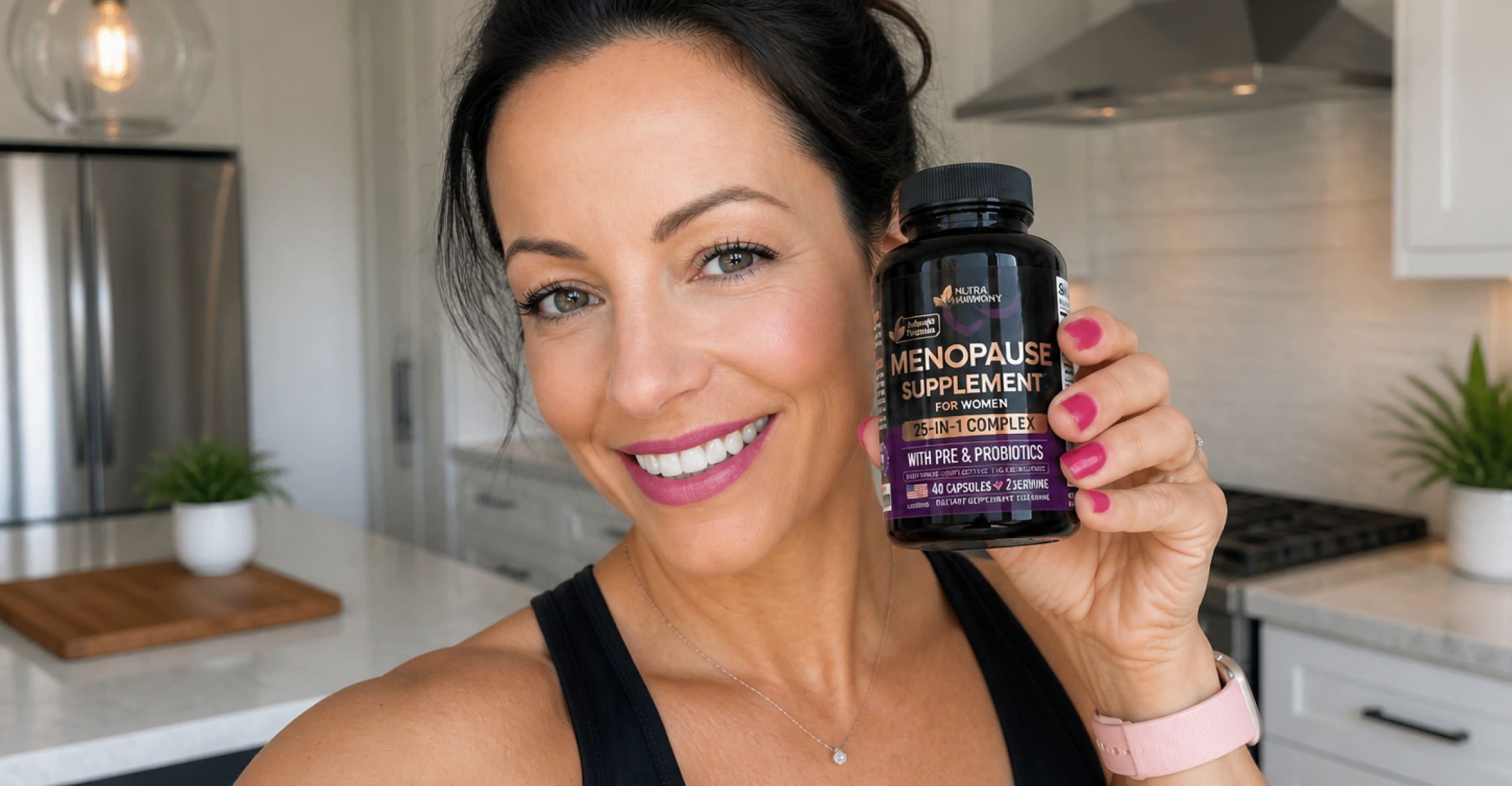 A smiling woman holds up a bottle of Nutra Harmony Menopause Supplement in her kitchen.