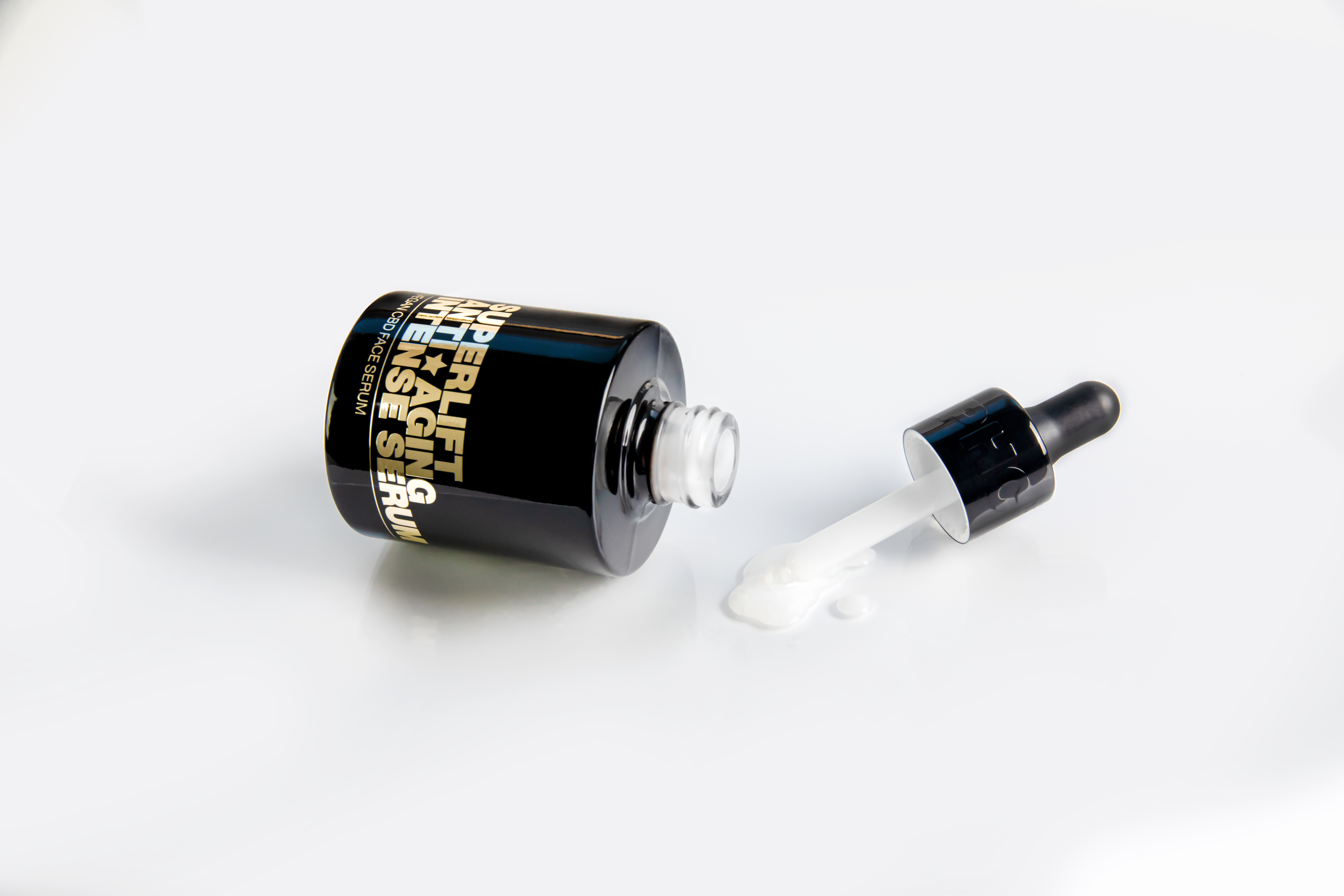 Black serum bottle with dropper, liquid spilled on white surface.