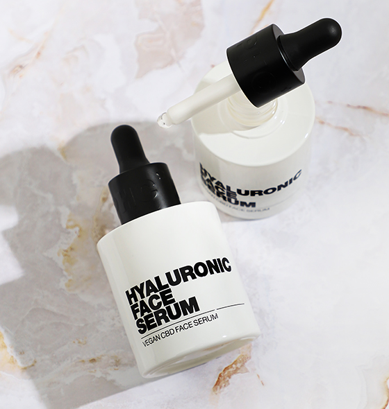 Two bottles of hyaluronic face serum with droppers on a marble surface.