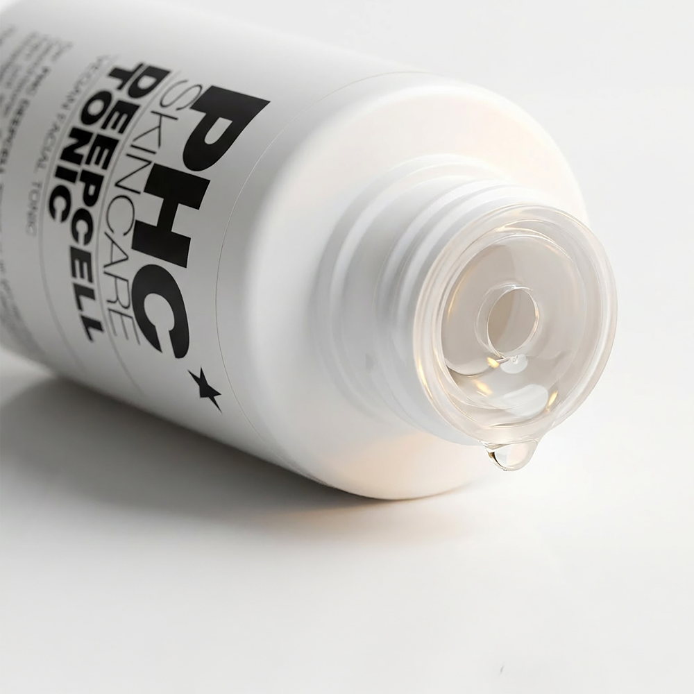 A close-up of a white bottle of PHC Skincare Deepcell Tonic, with a drop of clear liquid falling out.