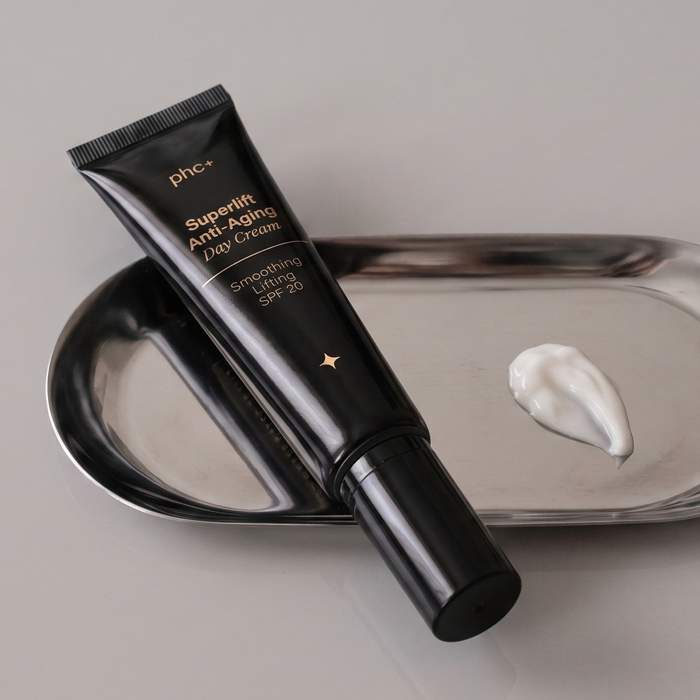 A black tube of phc+ anti-aging day cream on a silver tray with a swatch of the cream.