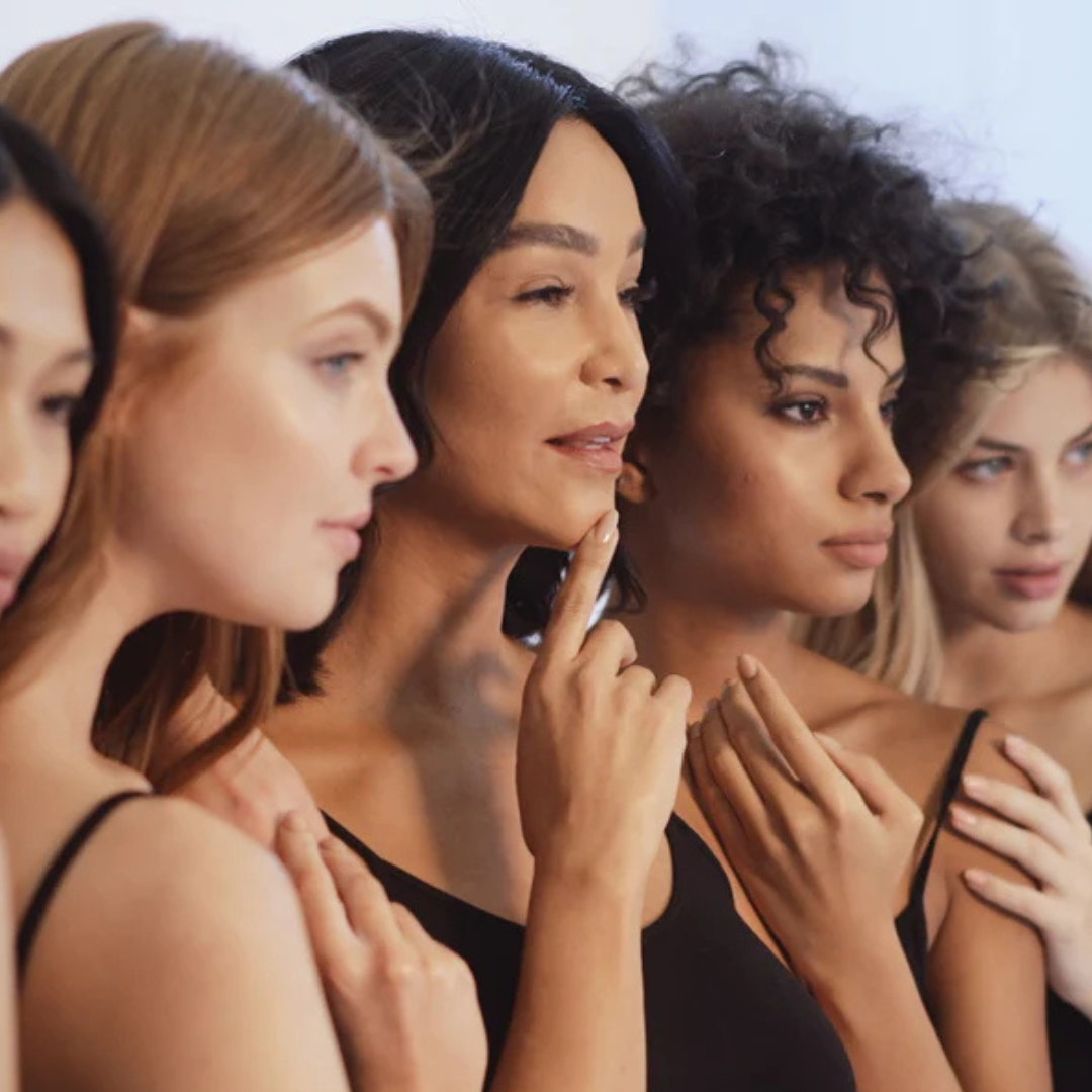 Five women in black tops posing together in profile view.