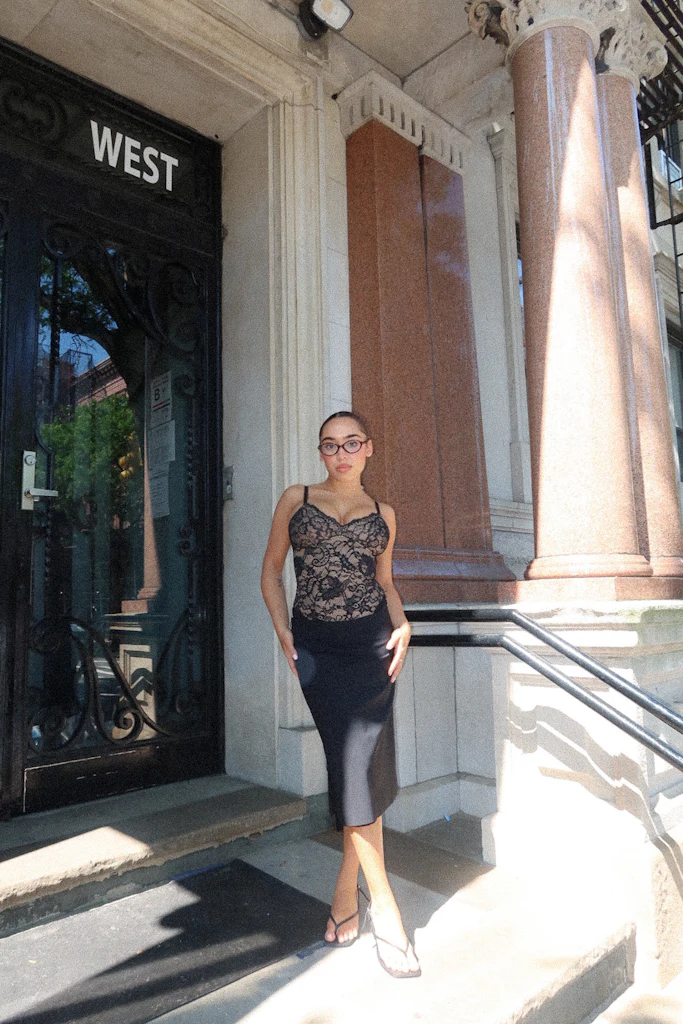 Person in black lace outfit standing by a building entrance labeled 'West.'