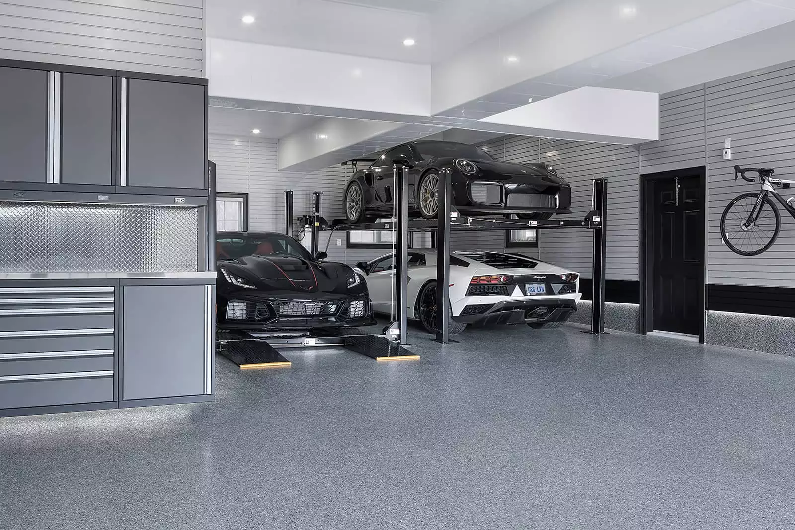 Modern garage with luxury cars on lifts and a bicycle on the wall.