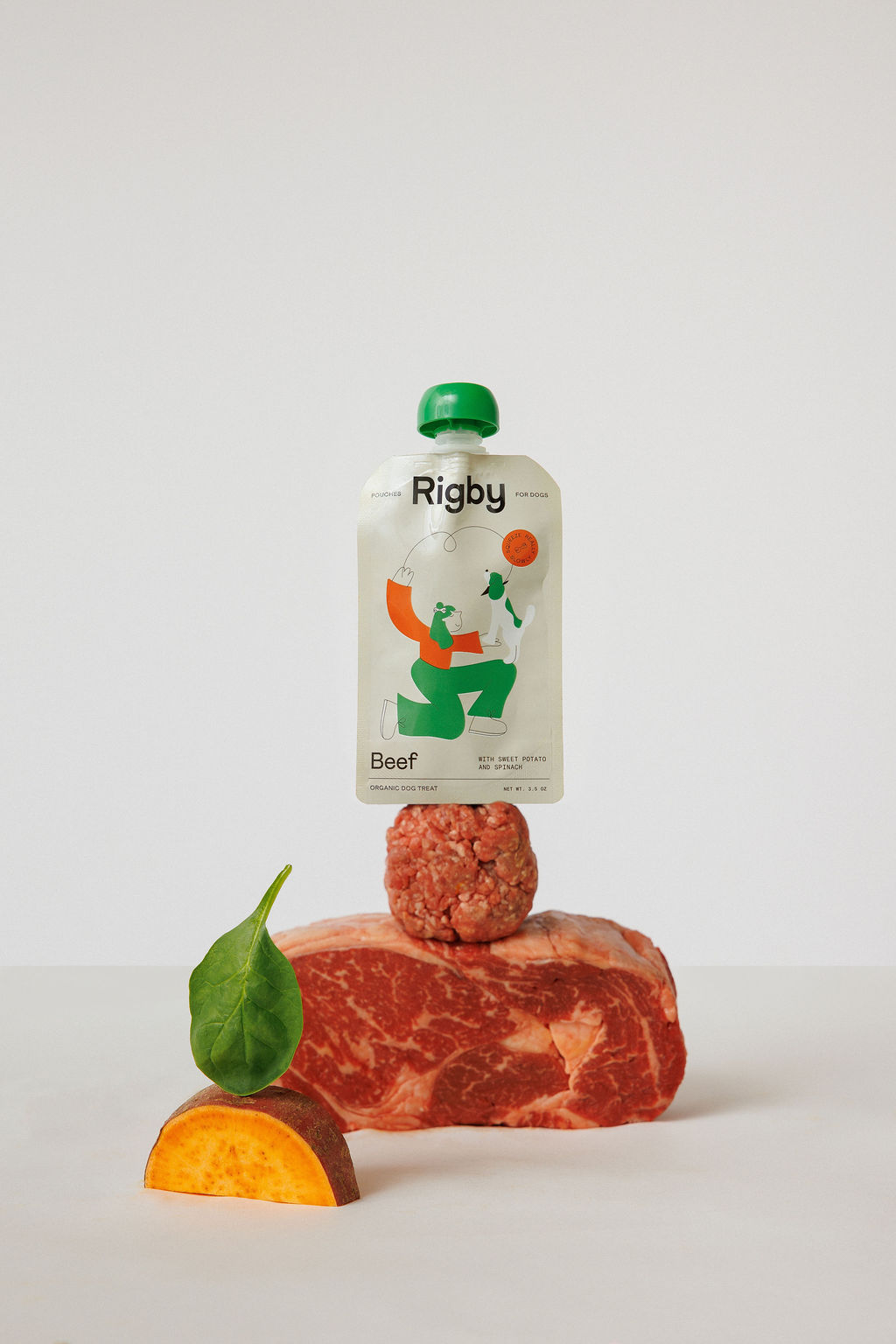 A pouch of Rigby beef dog treats stacked on its ingredients: beef, sweet potato, and spinach.