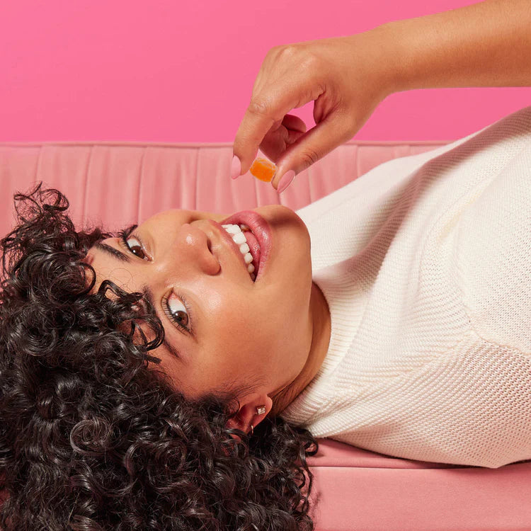 Person lying down, smiling, holding an orange gummy candy.