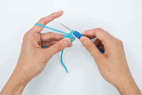 Hands holding a crochet hook and blue yarn in process of crocheting.
