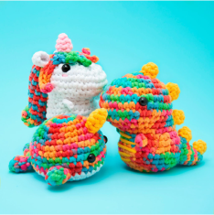 Colorful crocheted unicorn and dinosaur toys on a blue background.