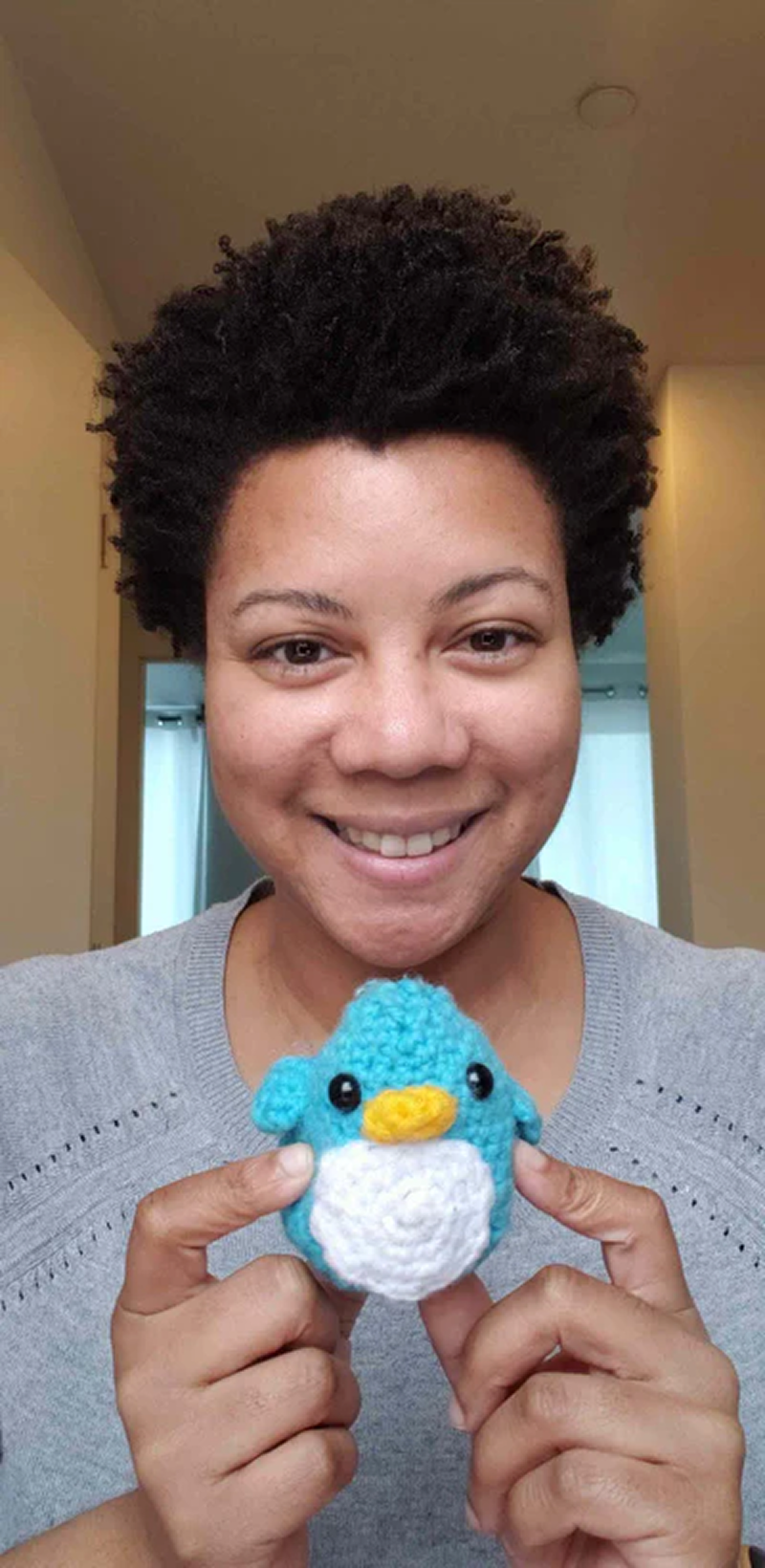 Person smiling, holding a small crocheted blue penguin.