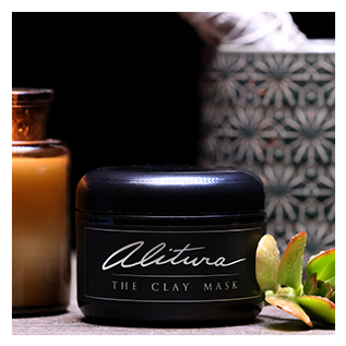 Black jar labeled 'Alitura The Clay Mask' on a surface with plants and a patterned object.