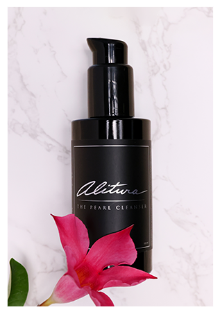 Black bottle of Alitura cleanser on marble with a pink flower.