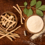 Herbal roots, powder, and leaves on a wooden surface.