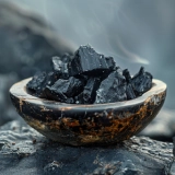 A bowl filled with charred, black chunks of wood on dark surface.