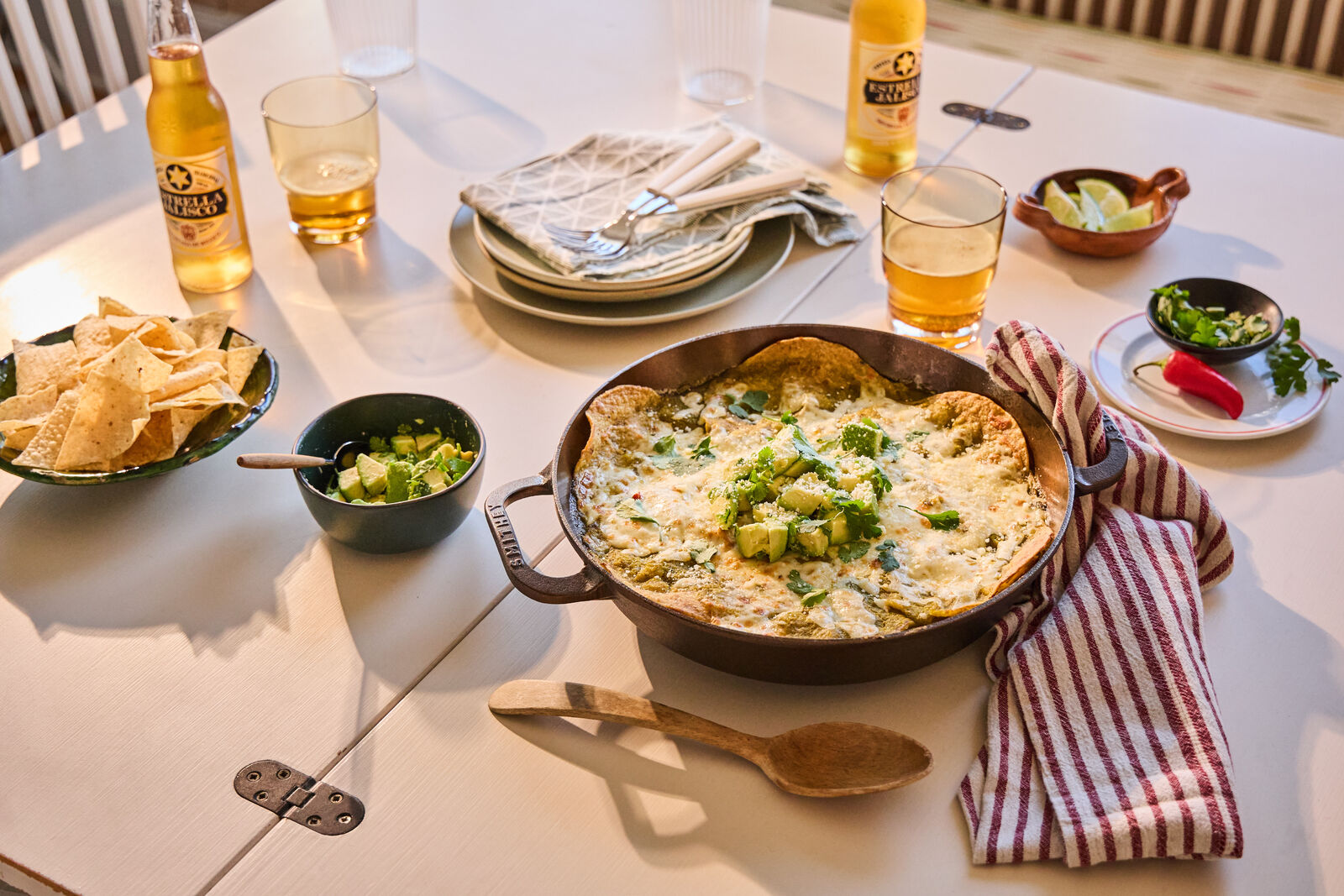 A table set with enchiladas, chips, garnishes, and beverages.