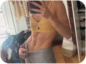 Person taking a mirror selfie, wearing a yellow top and gray pants, showing abdominal muscles.