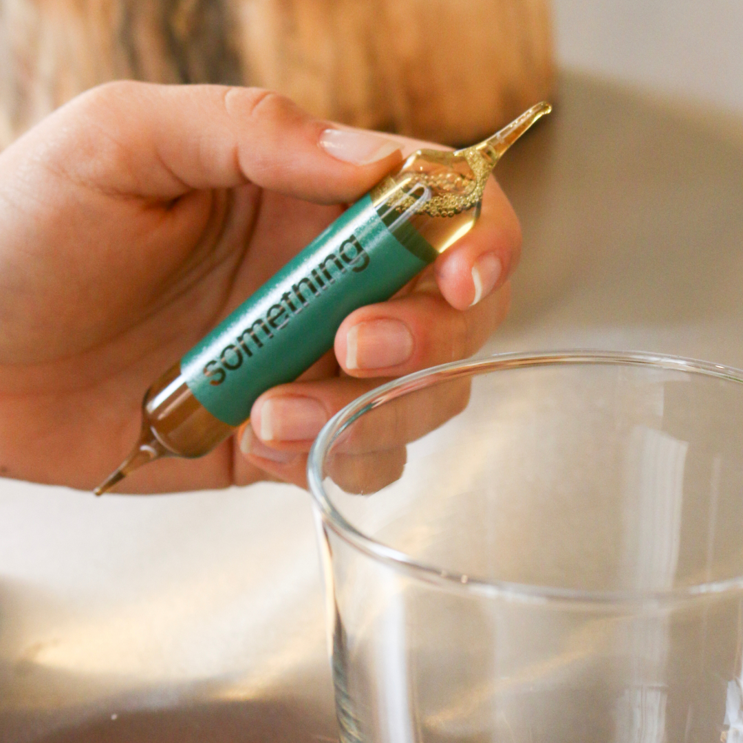 Hand holding a small vial labeled 'something' near a glass.