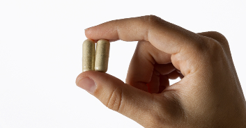 Hand holding two beige capsules against a white background.