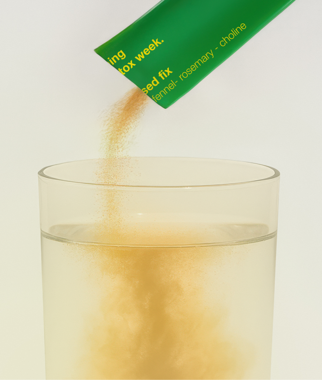 Orange powder being poured from a green packet into a glass of water.