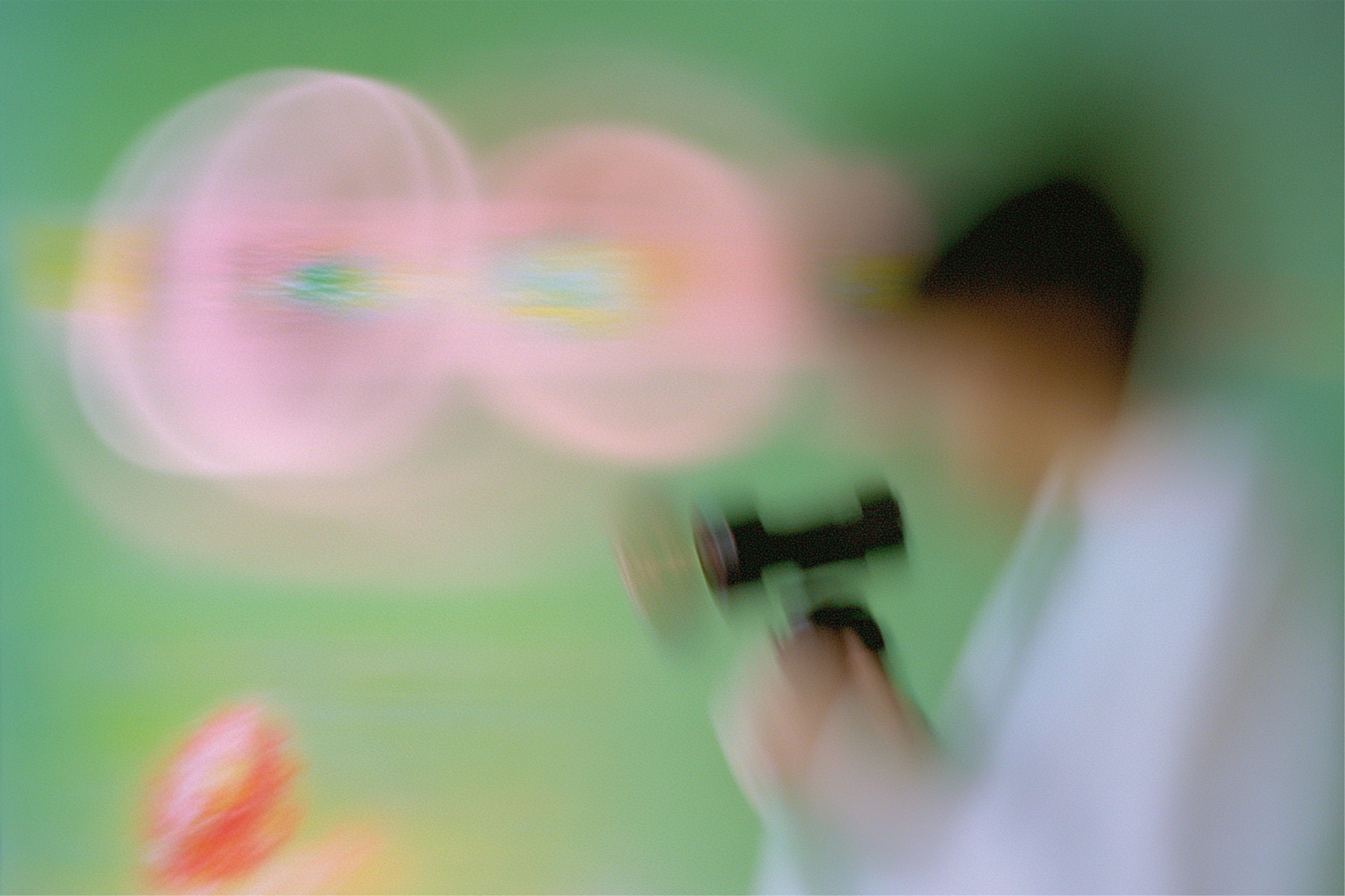 Blurry image of a person holding a camera against a green background.