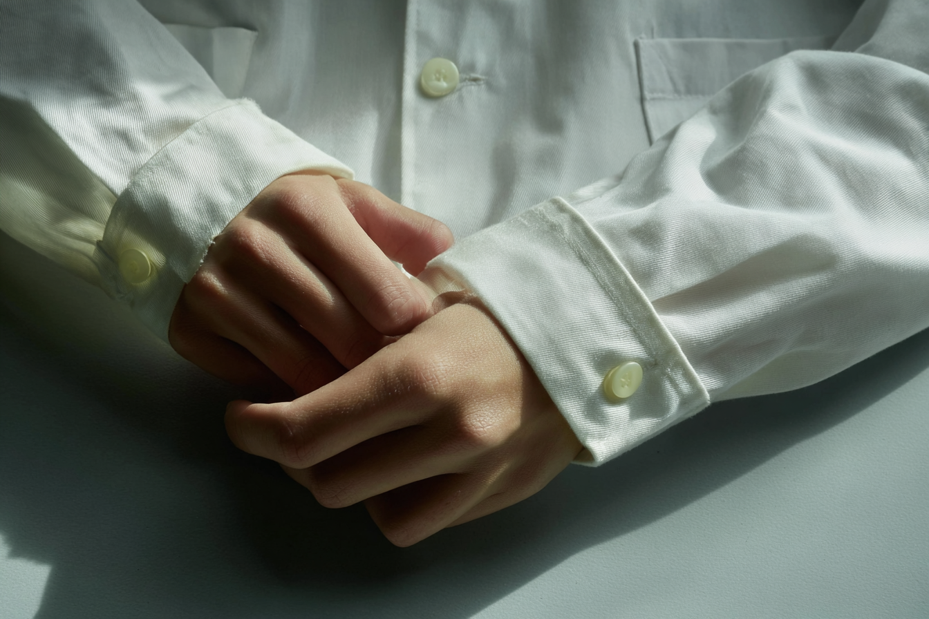 A close-up of a person in a white shirt with their hands clasped in front of them.
