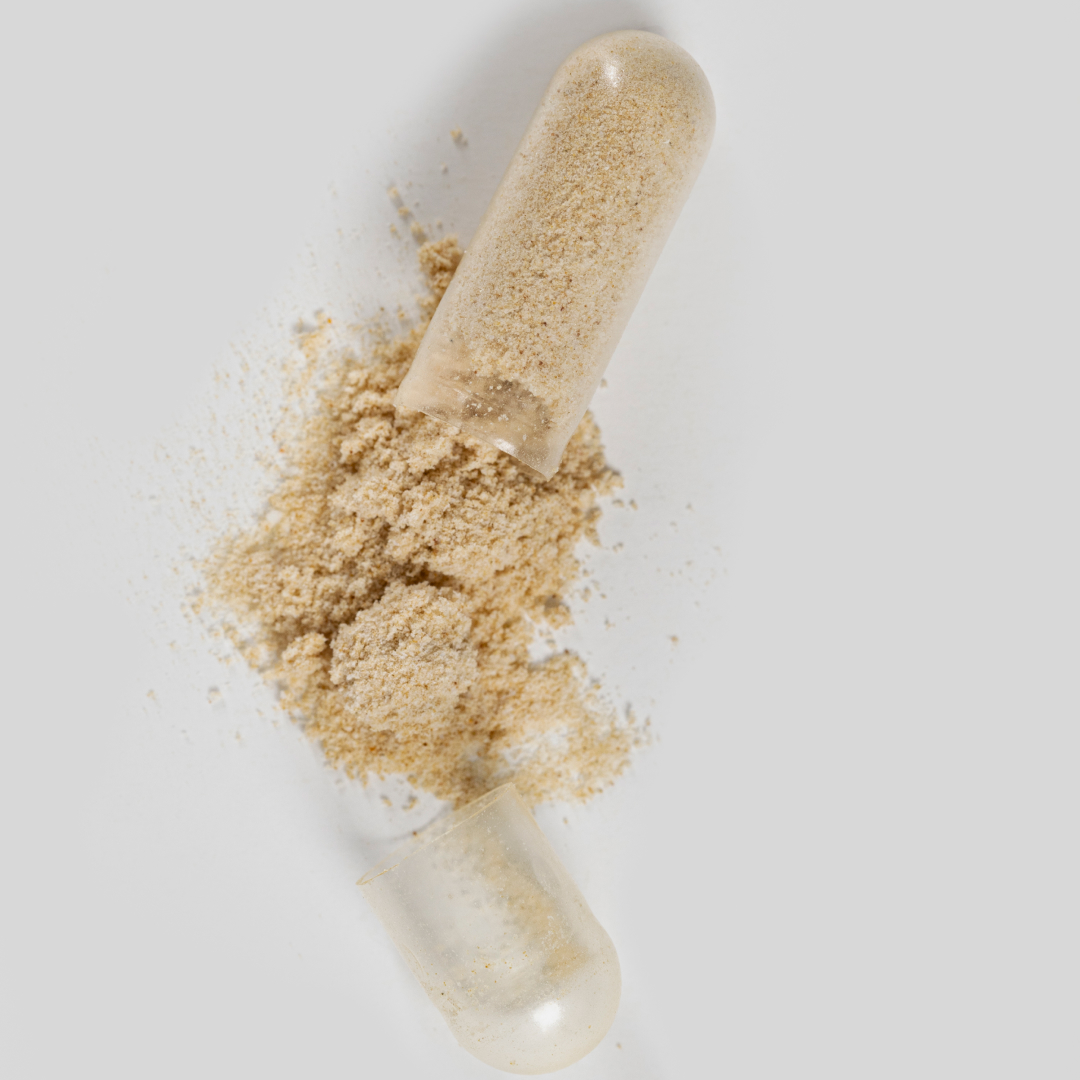 Open capsule with beige powder spilled out on white background.