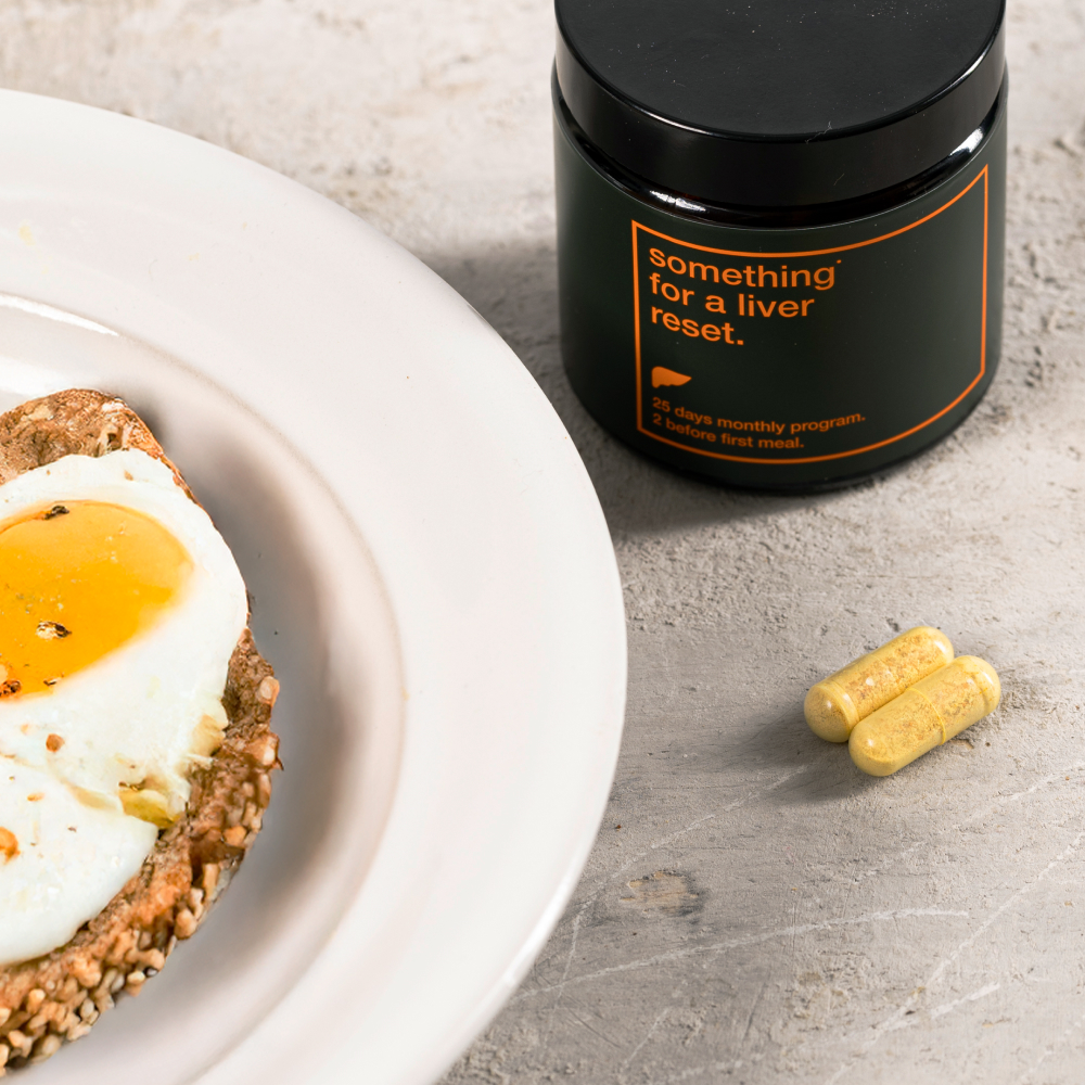 Plate with egg on toast, jar of liver supplement, and two yellow capsules.