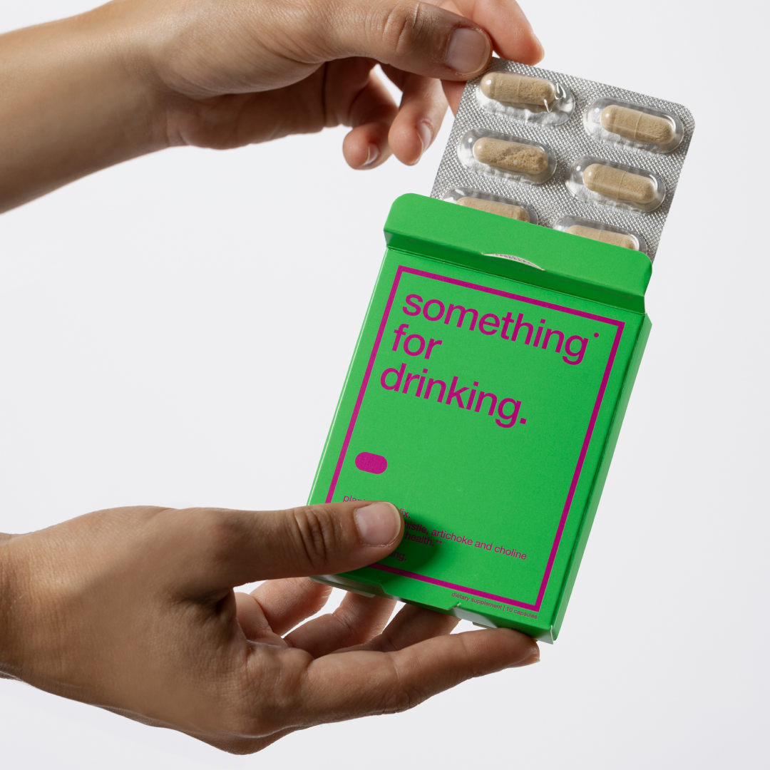 Hands holding a green box and blister pack of capsules.