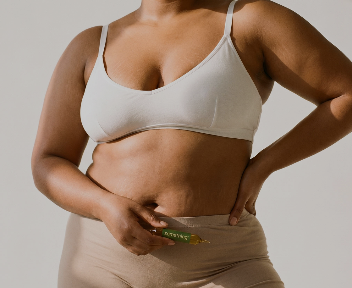 A person with visible stretch marks on their torso holds a small green vial against their stomach.