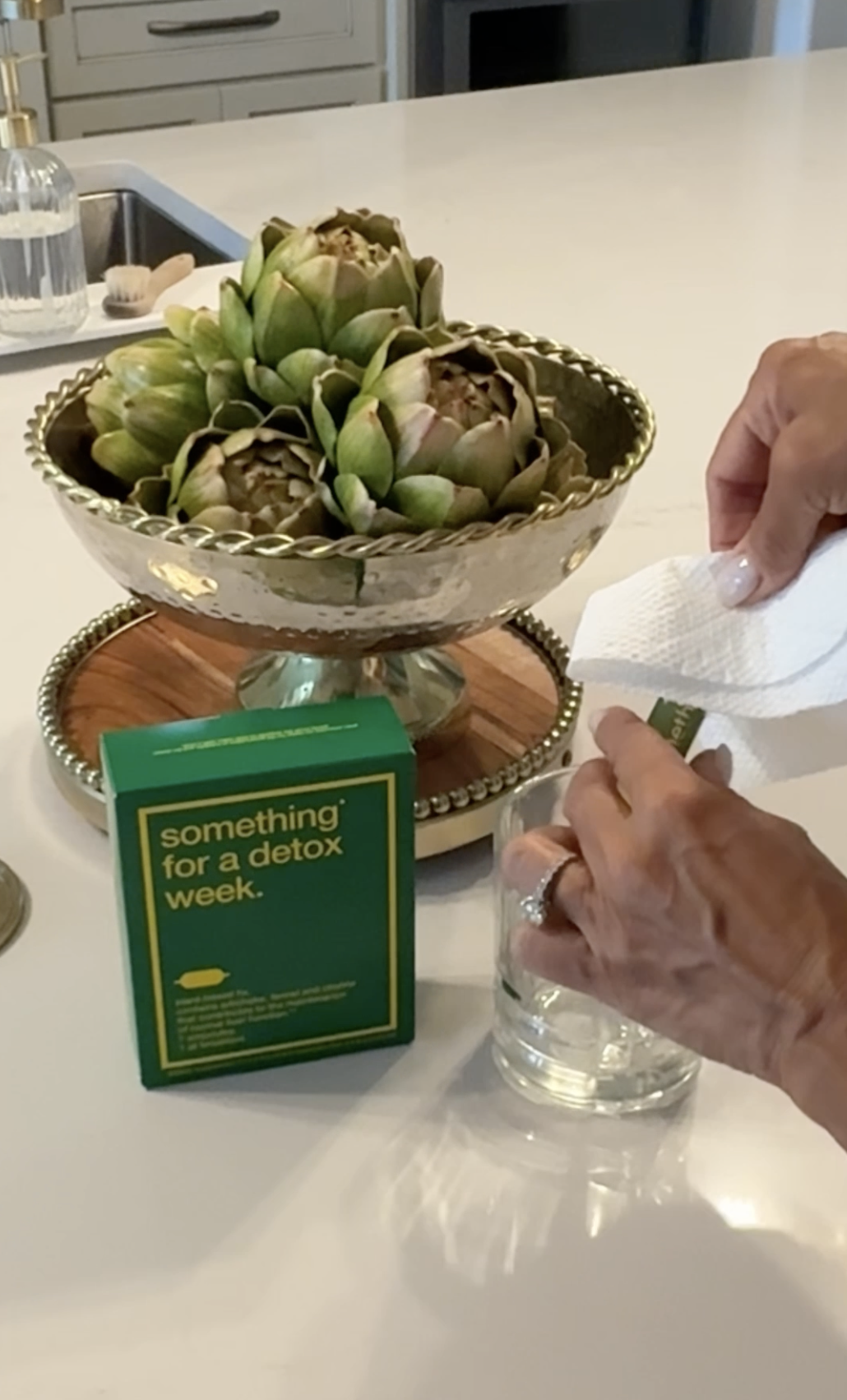 A person prepares a drink from a detox box on a kitchen counter with artichoke decor.