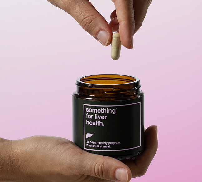 Hands holding a supplement jar labeled for liver health with a capsule above it.