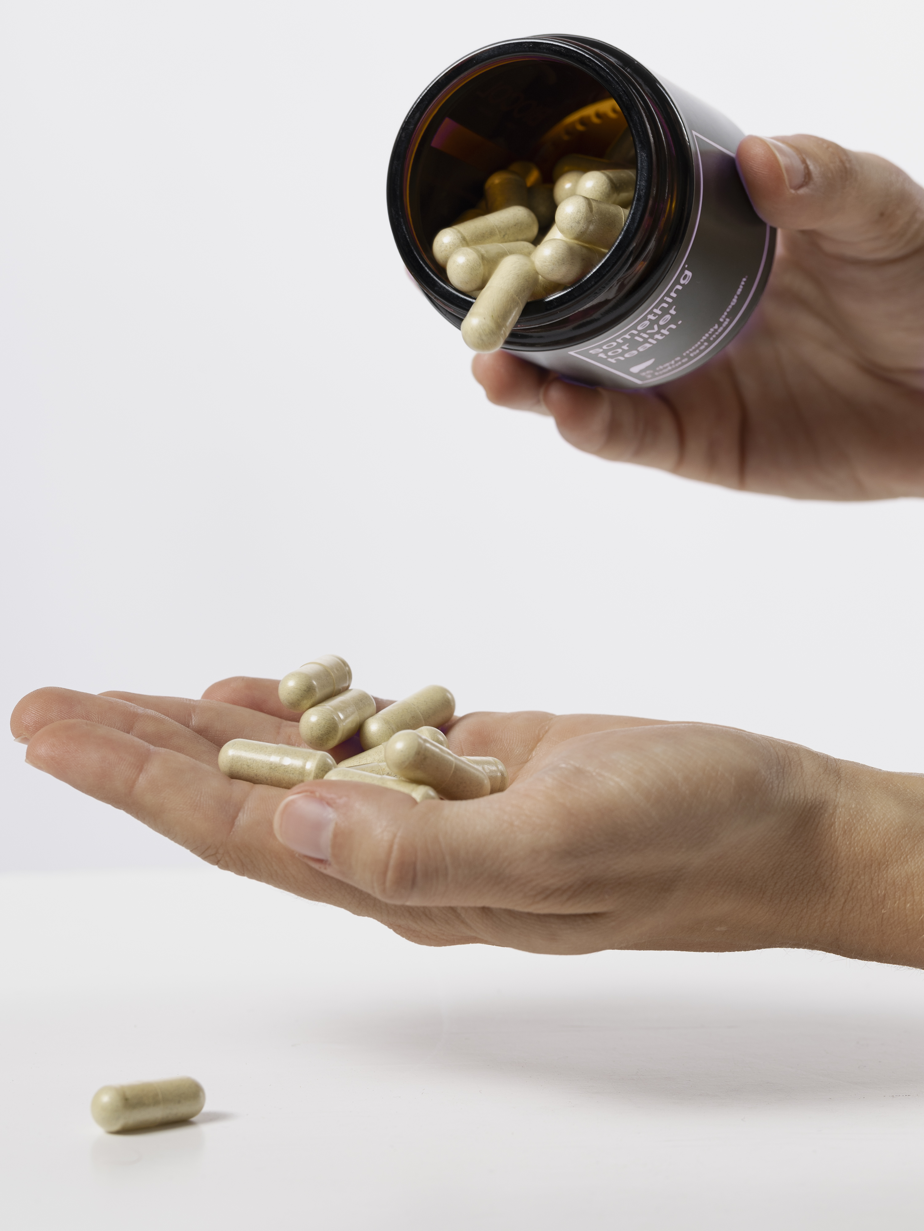 A person pouring capsules from a bottle into their hand against a white background.