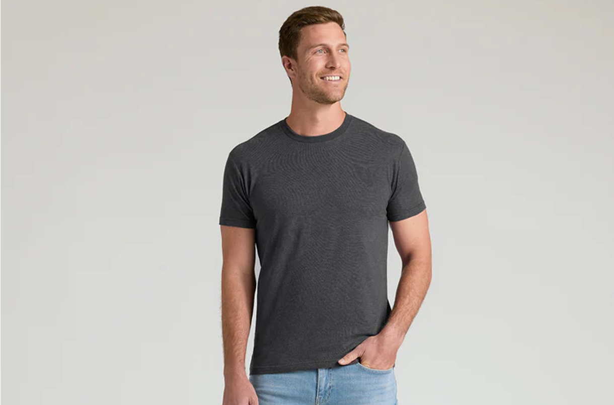 Man in a gray t-shirt and jeans smiling, standing against a plain background.
