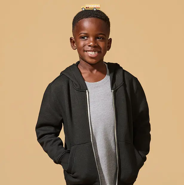 Smiling child with a toy school bus on their head, wearing a black hoodie.