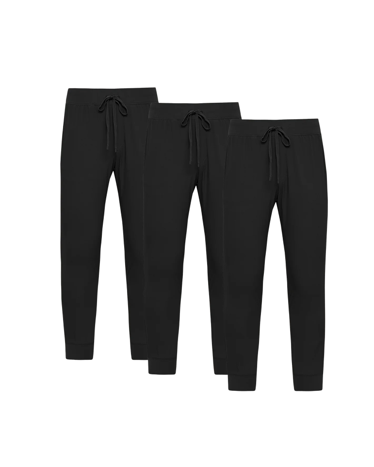 Three pairs of black joggers with drawstrings against a black background.