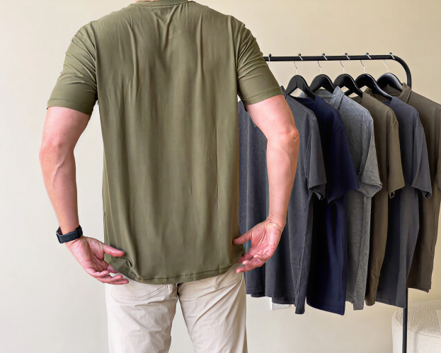 Person wearing a green shirt, standing next to a rack of various colored shirts.