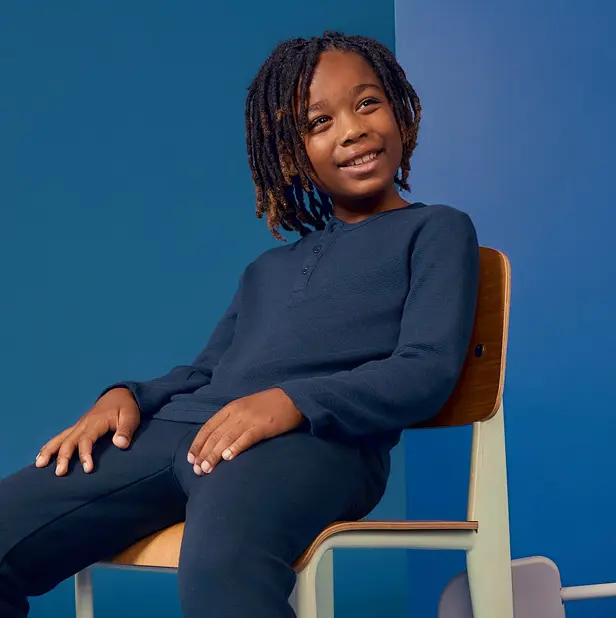 Child sitting on a chair against a blue background, smiling.