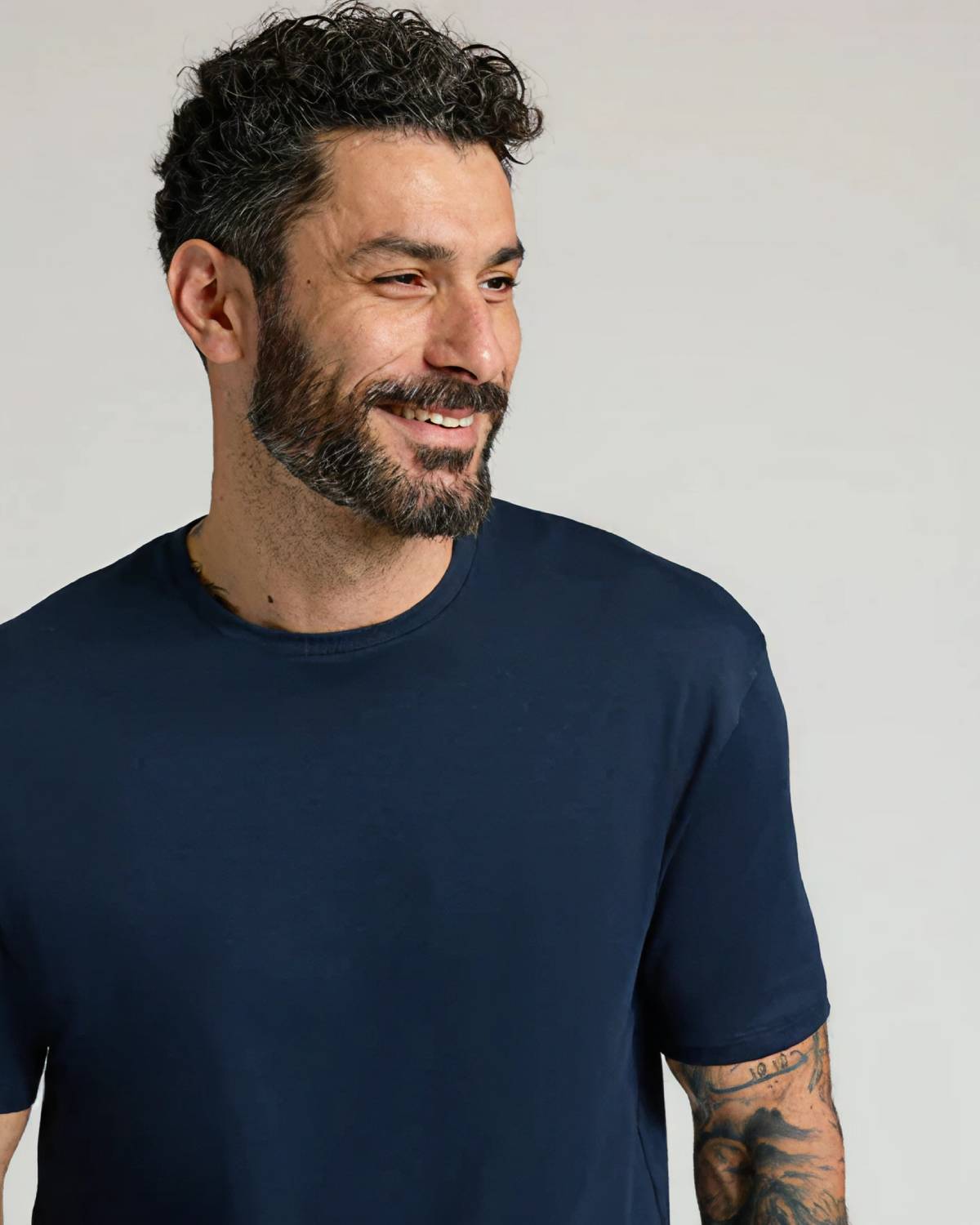 Man with curly hair and beard wearing a navy blue t-shirt, smiling.