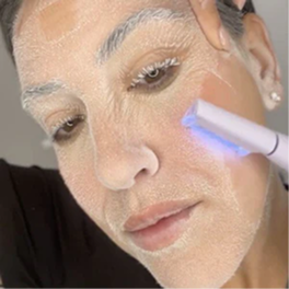 Person applying skincare treatment with a device emitting blue light.