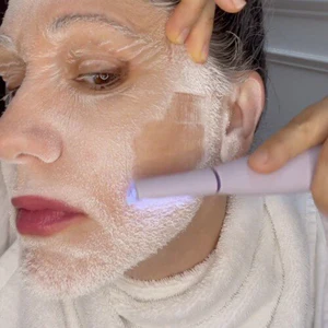 A person applies a face treatment with a handheld device.
