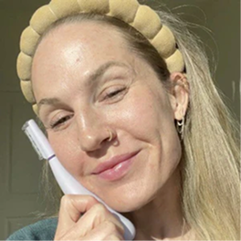 Person smiling while holding a facial care device next to their cheek.