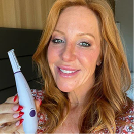 Person holding a white device, smiling in a room.