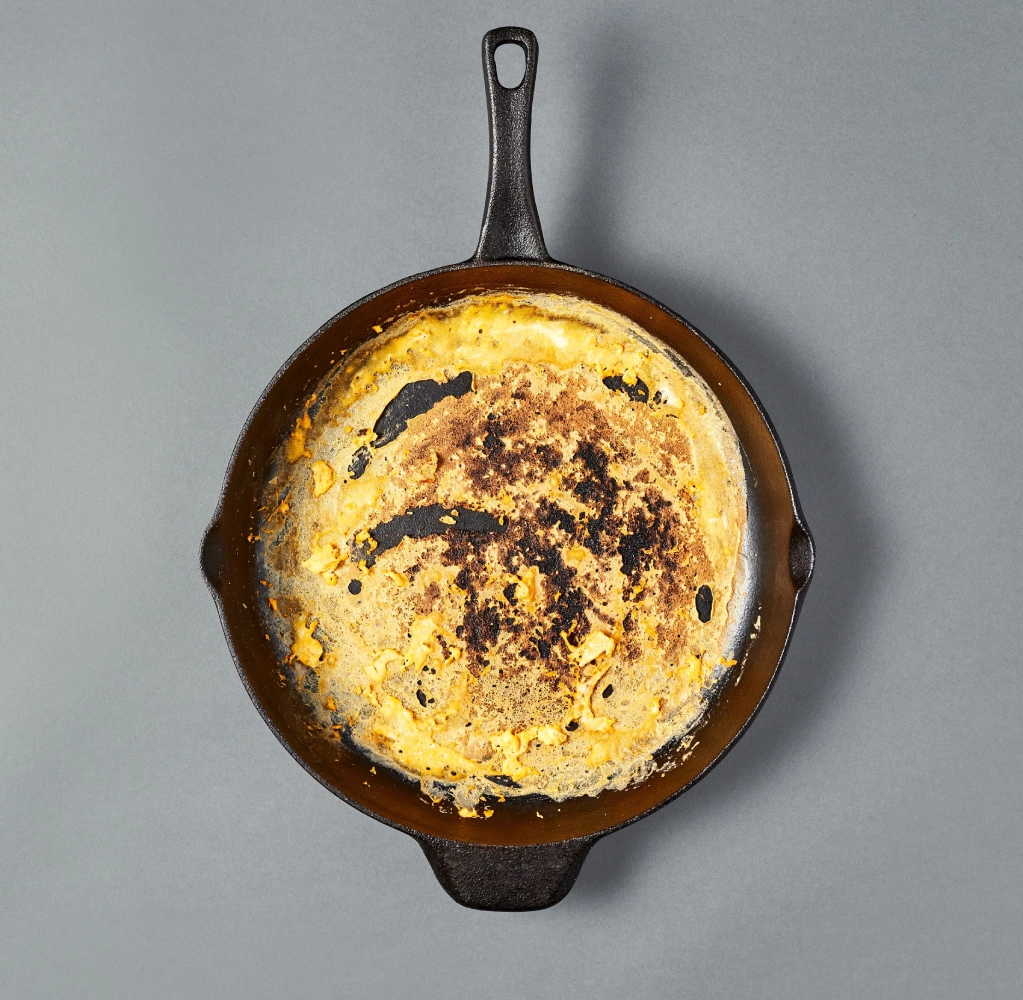A black frying pan with cooked food residue on a gray background.