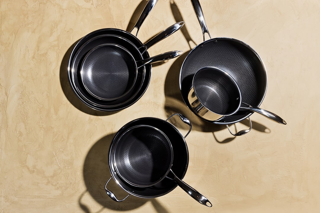 Three stainless steel pots and pans on a beige surface.
