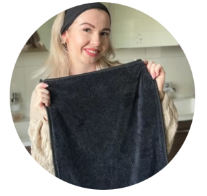 A smiling woman with blonde hair and a black headband holds up a dark grey towel.