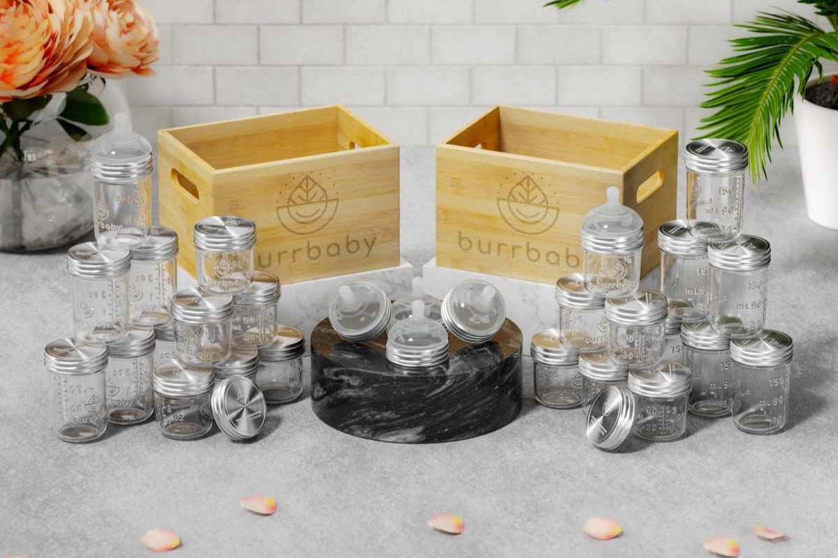 Glass jars with silver lids, wooden boxes, and flowers on a gray surface.