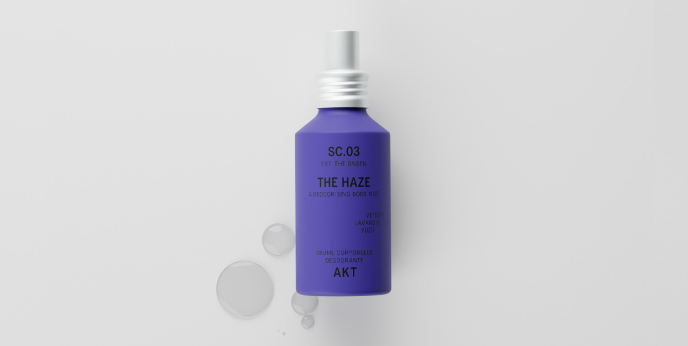 A purple bottle with a white applicator tip sits on a white surface next to several clear droplets.