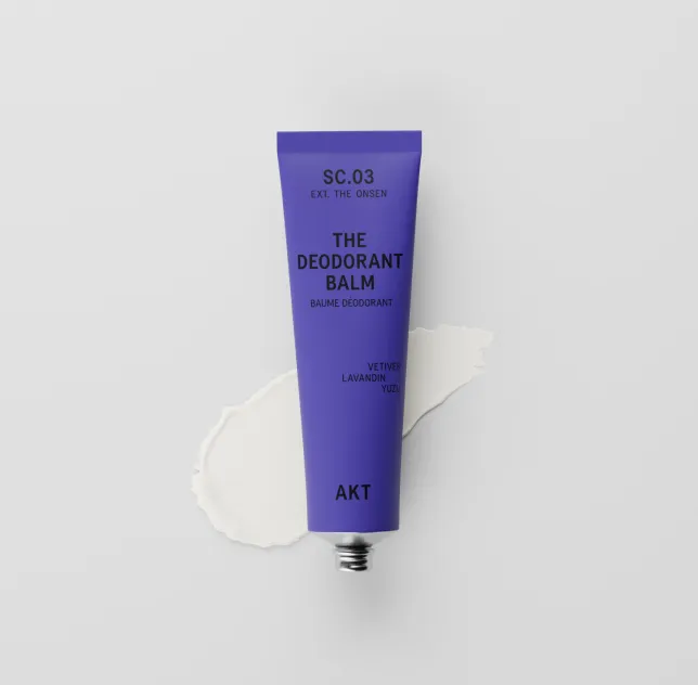 A purple tube of AKT The Deodorant Balm lies on a swatch of white cream.