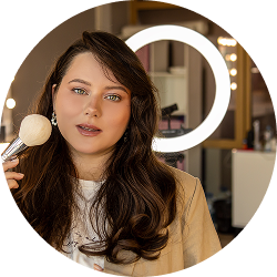 Person holding a makeup brush in front of a ring light.