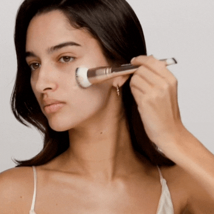 Person applying makeup with a brush on their cheek.